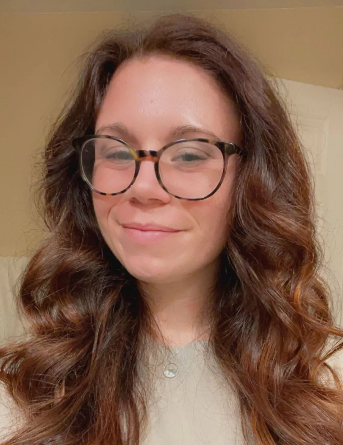 Morgan LaDuca smiling, in round tortoiseshell glasses and a cream sweater, with long brown hair over the shoulders